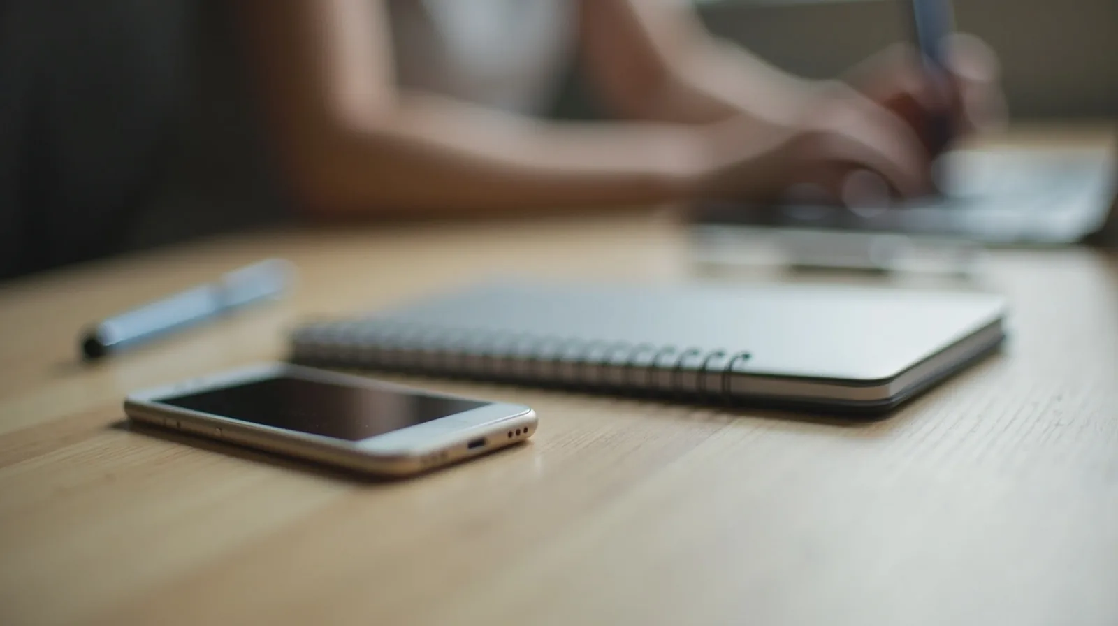 A close-up of a phone face-down on a desk with a notebook, deliberately set aside during work