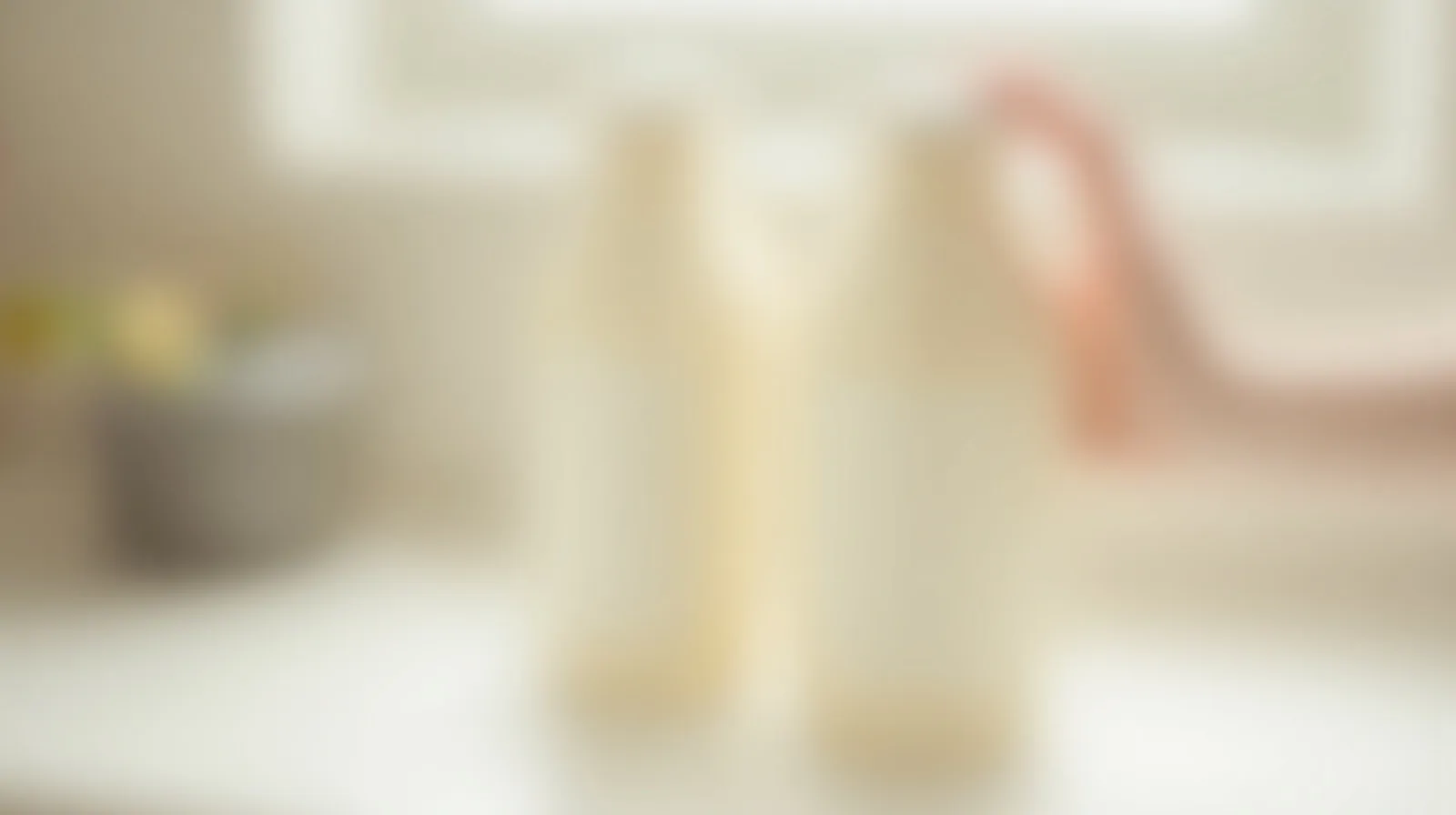 Two nearly identical unlabeled bottles side by side on a bright kitchen counter, a hand reaching for one