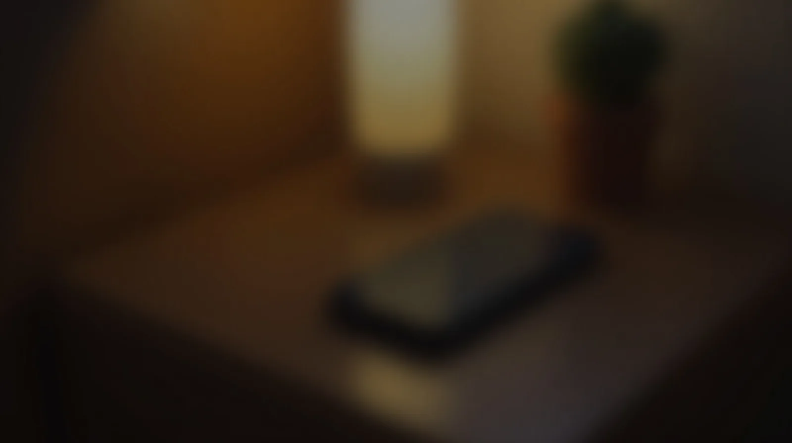 A close-up of a phone charging on a wooden nightstand beside a warm lamp