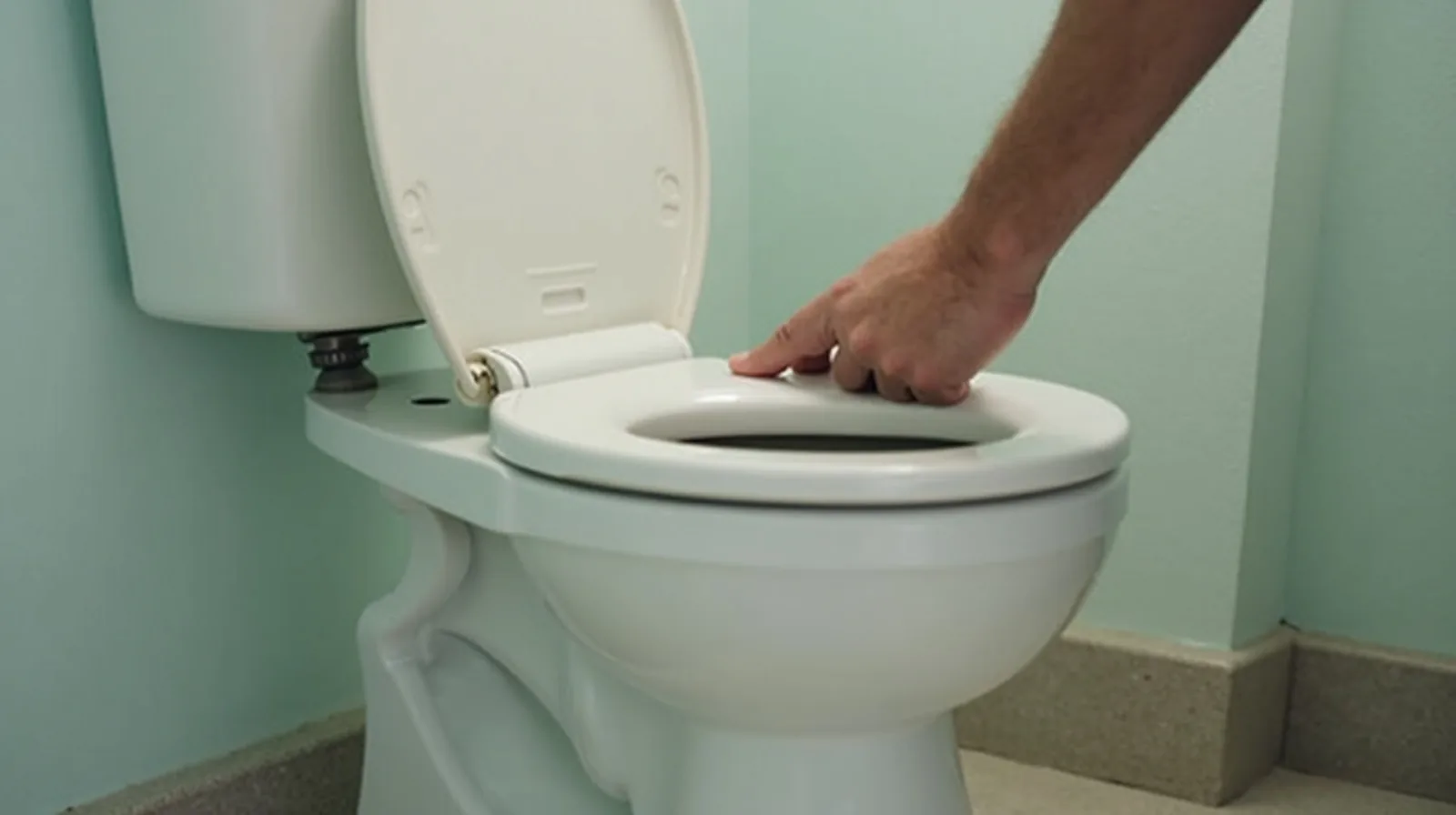 A person in profile lifting the lid off a toilet tank to check for a silent leak in a bright bathroom