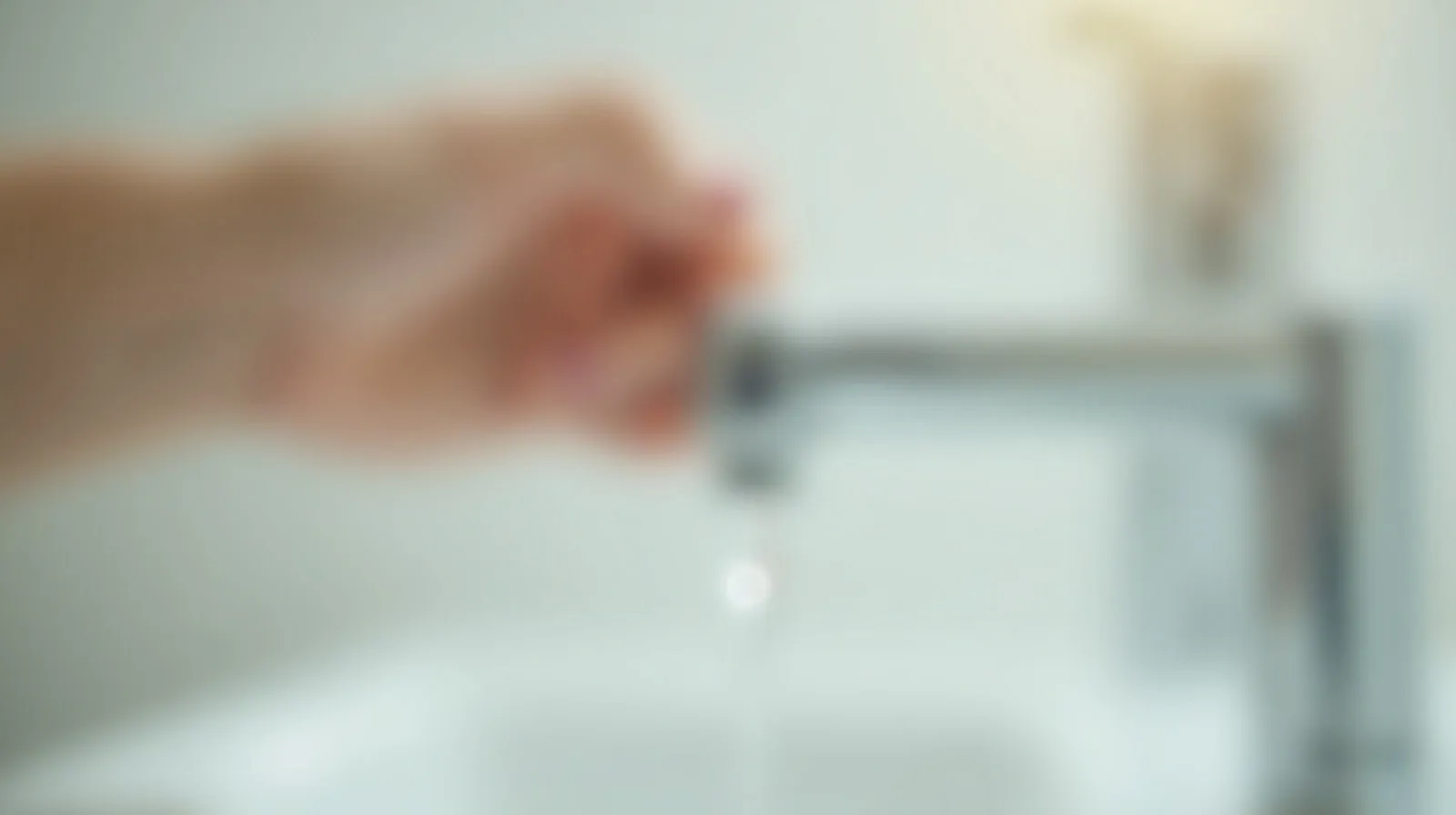A close-up of a dripping faucet with a single droplet caught mid-fall in bright bathroom light